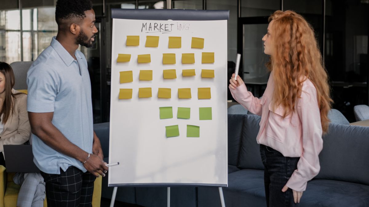 Dos personas debatiendo un proyecto con notas adhesivas en un panel